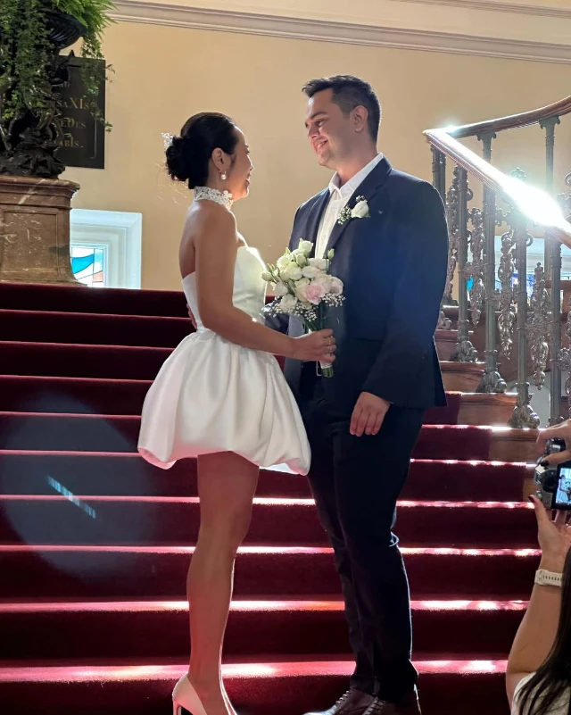 Bride in a short made-to-measure dress with her groom on red-carpeted steps