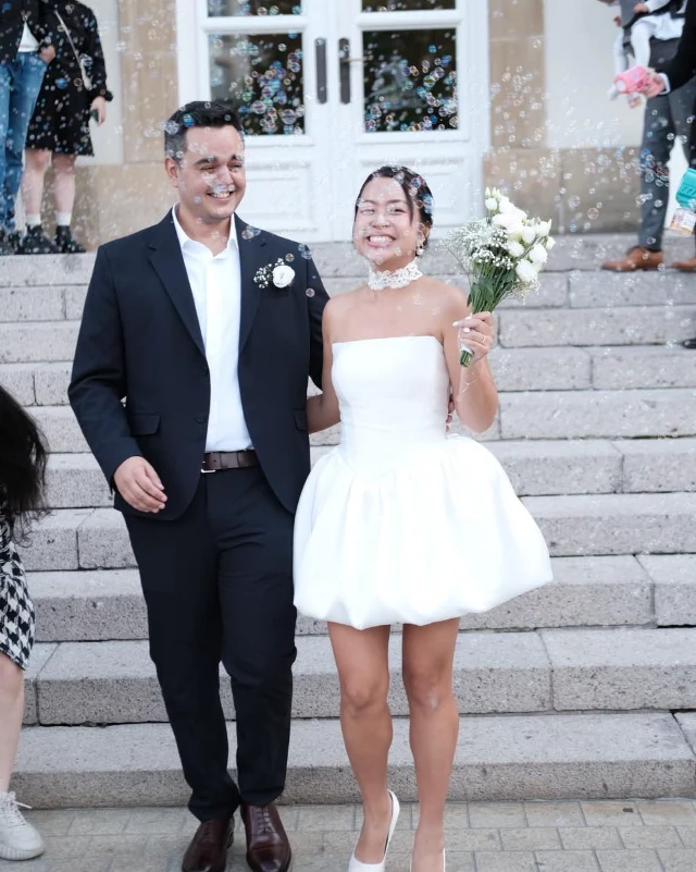 Váy chụp ảnh cưới: chọn phom và chất liệu để lên hình đẹp Cô dâu và chú rể đứng trên bậc thềm đá, thấy rõ dáng xoè của váy trắng ngắn