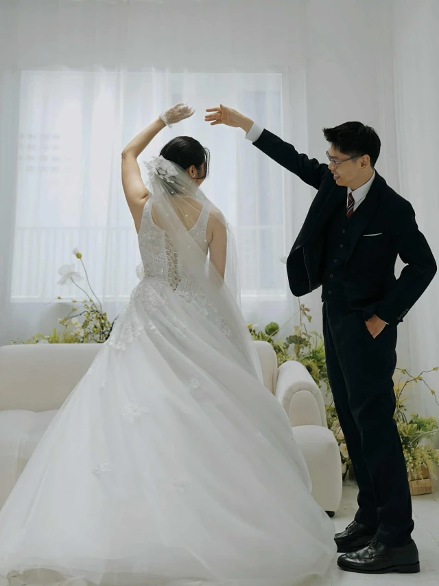 Dâu giơ tay xoay người khoe phần lưng váy, chú rể đưa tay đỡ trong phòng chụp