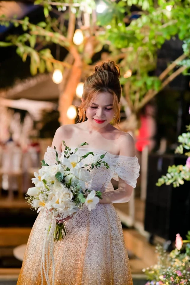 Dâu ôm bó hoa trắng dưới ánh đèn vàng, thân váy ombre ren kim tuyến lấp lánh, tay áo trễ vai